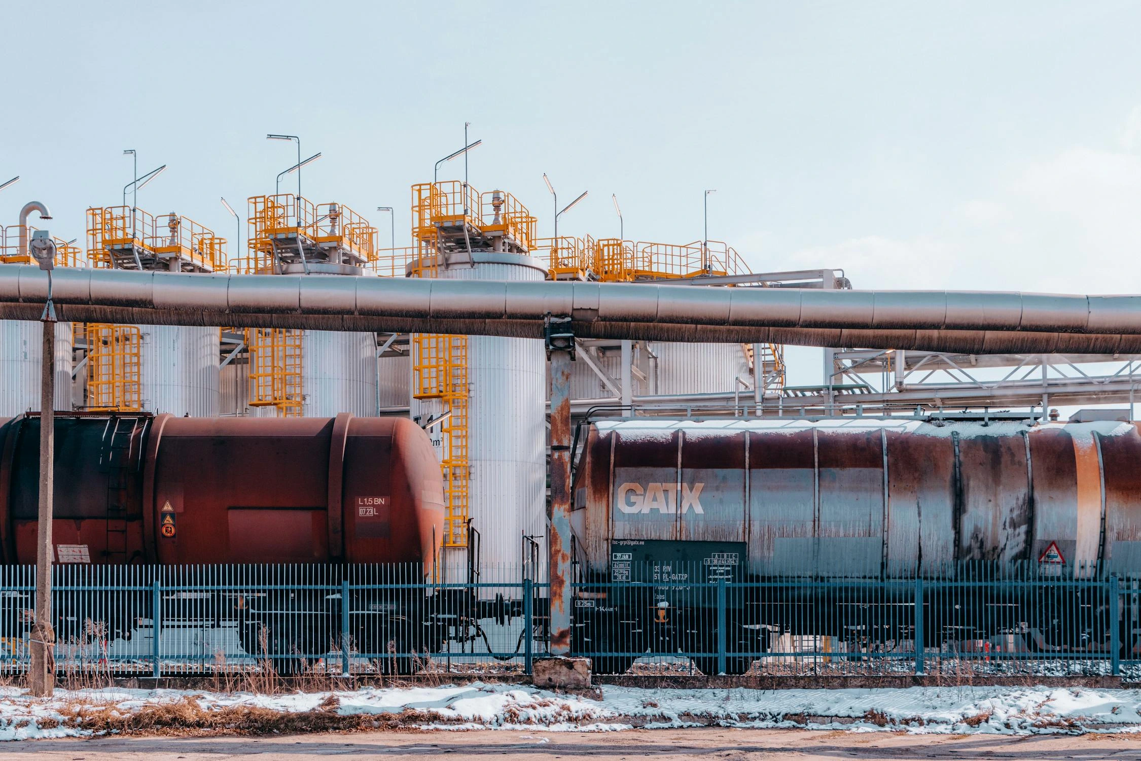 An industrial area with large upright tanks and a pipe going from left to right.